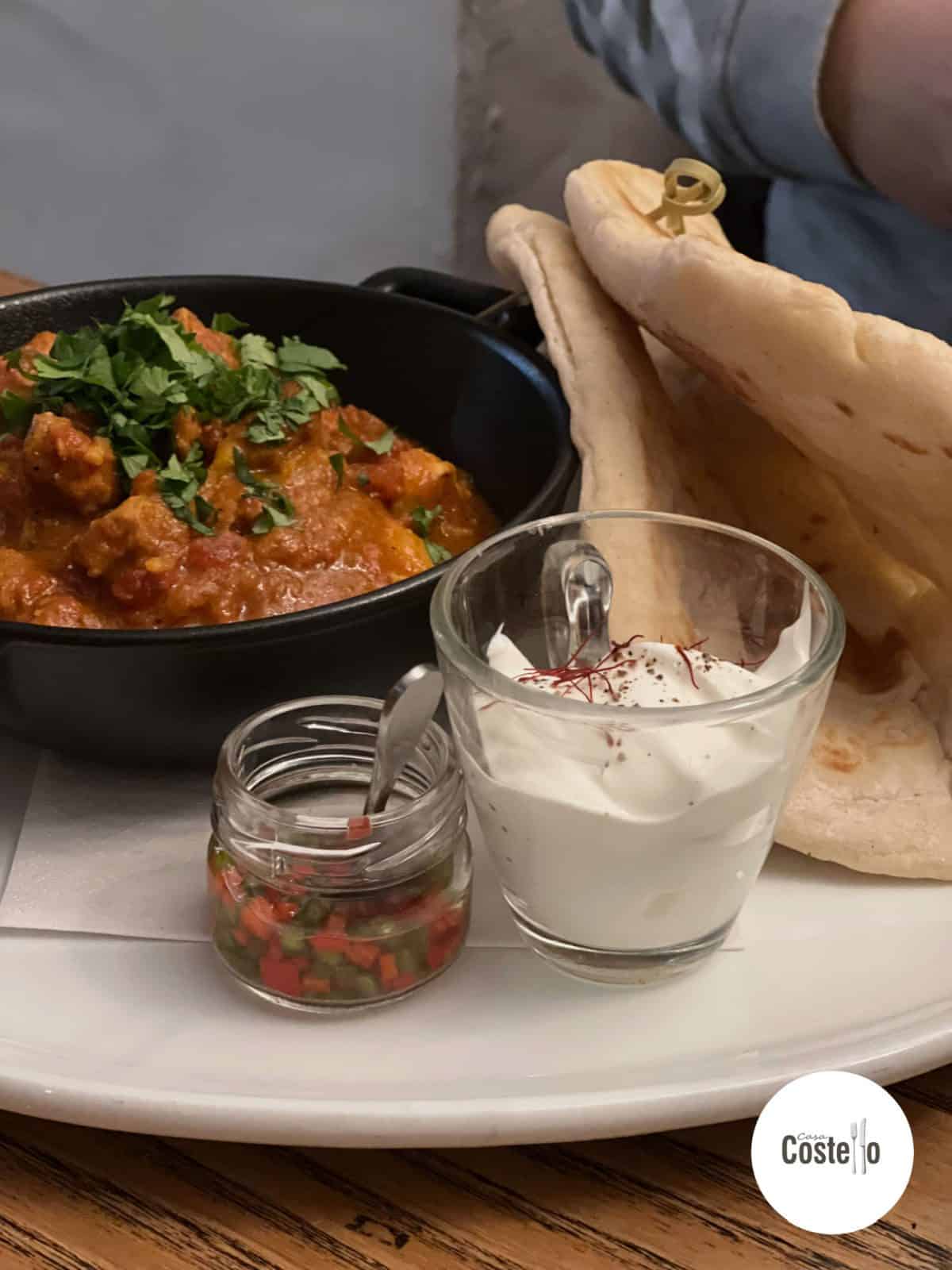 Portion of curry with separate jar of chillies, sour cream and naan bread on the side
