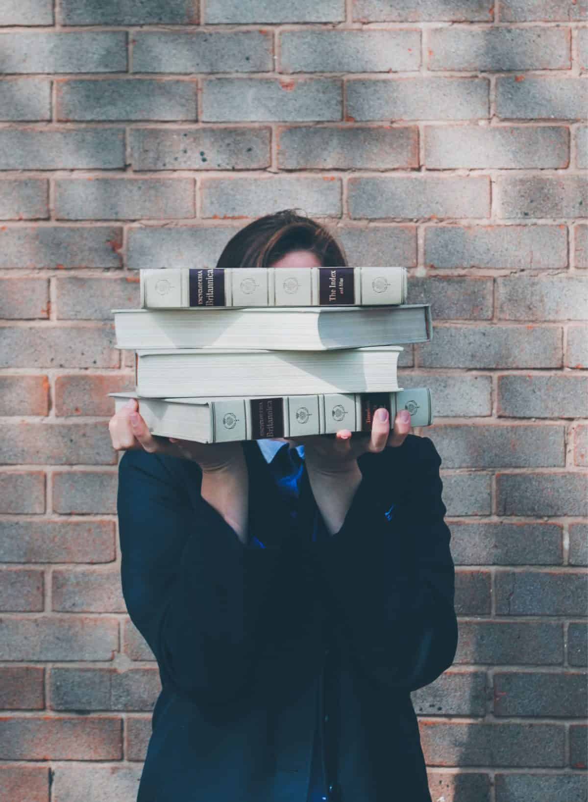 Female holding up 4 large textbooks in front of her face