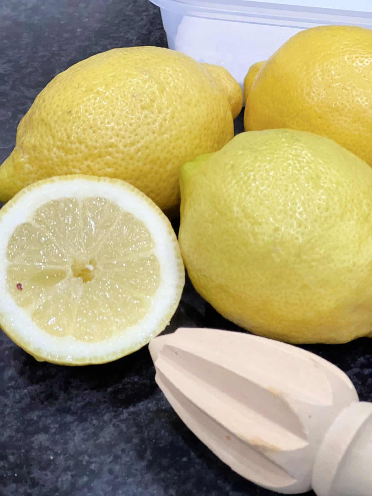 3 whole lemons and one cut in half with a wooden squeezer on a worktop
