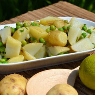 White plate with a no mayo potato salad with lime and mint dressing. The image shows raw potatoes and a wooden spoon in the foreground.